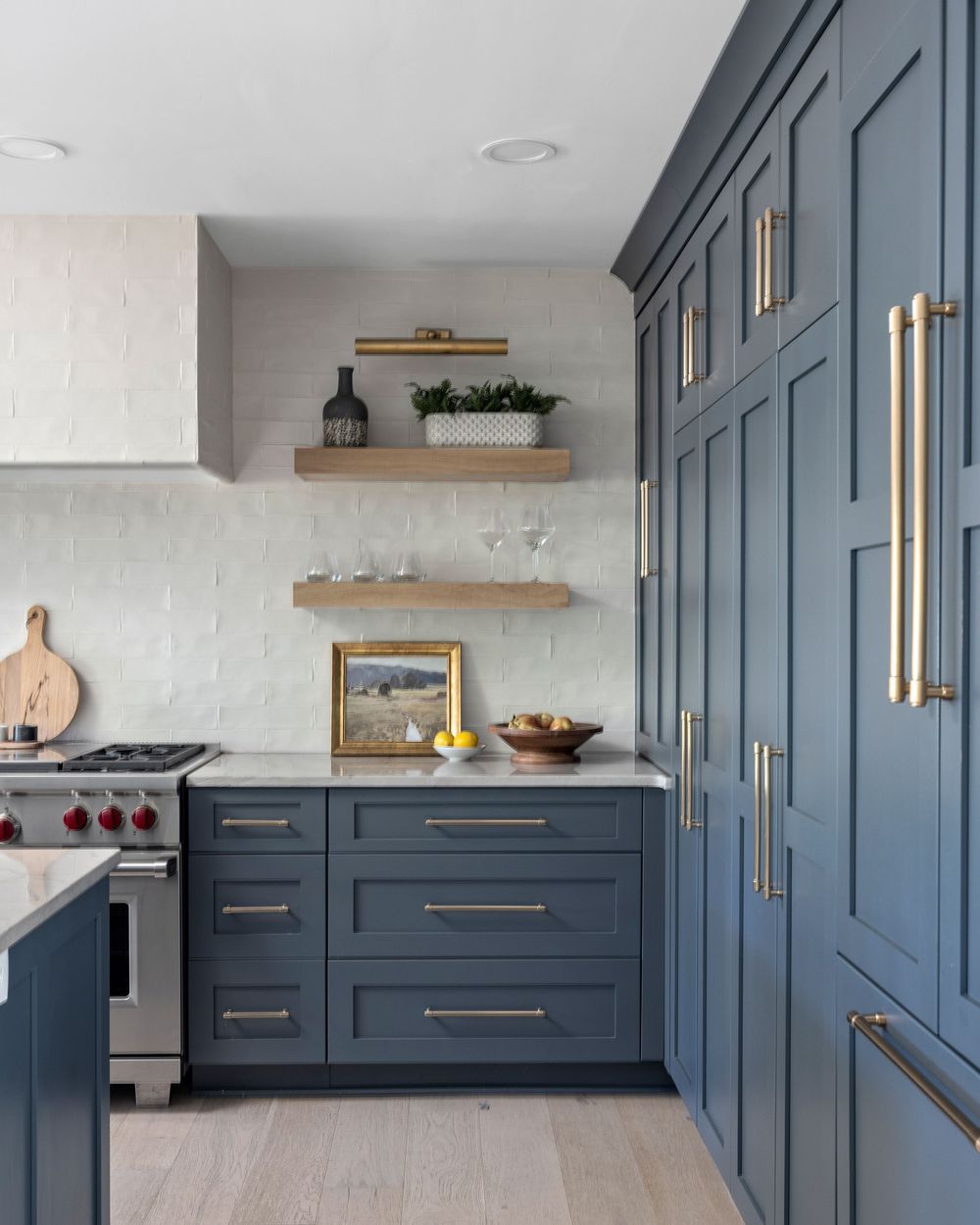 Slate blue kitchen with brass hardware and oak shelves